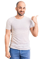 Sticker - Young handsome man wearing casual t shirt smiling with happy face looking and pointing to the side with thumb up.