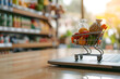 © Seegraphie - Digitales Einkaufen im Miniaturformat: E-Commerce-Konzept mit Mini-Einkaufswagen und Laptop, gefüllt mit verschiedenen Waren