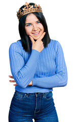 Poster - Young brunette woman with blue eyes wearing princess crown looking confident at the camera smiling with crossed arms and hand raised on chin. thinking positive.