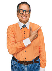 Canvas Print - Middle age indian man wearing casual clothes and glasses cheerful with a smile of face pointing with hand and finger up to the side with happy and natural expression on face