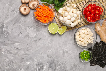 Cooking delicious ramen soup. Different ingredients on gray textured table, flat lay. Space for text