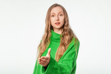 Wall Mural - Nice to meet you. Friendly smiling woman in green sweater stretching her hand welcoming guests, hospitality. Indoor studio shot isolated on white background