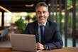 © kimly - Portrait of mature Indian or Latin business man ceo trader using laptop computer, typing, working in modern office. Middle-age Hispanic smiling handsome businessman entrepreneur looking at camera