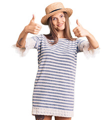 Canvas Print - Beautiful caucasian woman wearing summer hat approving doing positive gesture with hand, thumbs up smiling and happy for success. winner gesture.