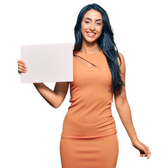 Wall Mural - Beautiful hispanic woman holding blank empty banner looking positive and happy standing and smiling with a confident smile showing teeth