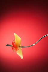 Wall Mural - Fork with pasta and tomato on a red background