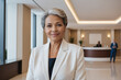 © EliteLensCraftImages - female old age multiracial hotel receptionist or manager standing in lobby with reception. welcoming guests, offering services or checkin. tourism and travel concept.