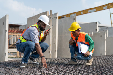 Foreman and laborer checking steel reinforcement cage for making precast concrete wall in construction site. Workers wearing vest and helmet safety working construction site.