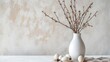 White ceramic vase with spring branches, some eggs laying in front of vase on a table. Wall backdrop. Copy space. Minimalistic, nordic spring decoration. Late winter feeling. Neutral, natural colors.