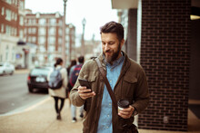 Man Walking With Coffee And Using Smartphone In City Street