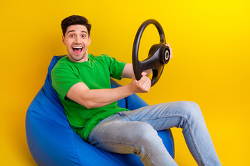 Sticker - Full size photo of impressed guy wear t-shirt sit on bean bag holding steering wheel driving car isolated on yellow color background