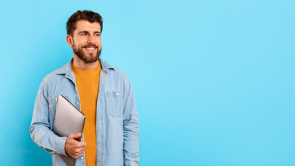 Happy young man holding his laptop computer on blue background