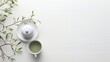  a cup of green tea next to a white teapot on a saucer and a branch of a tree.