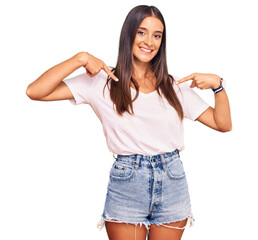 Wall Mural - Young hispanic woman wearing casual white tshirt looking confident with smile on face, pointing oneself with fingers proud and happy.