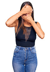 Wall Mural - Young hispanic woman wearing casual clothes covering eyes and mouth with hands, surprised and shocked. hiding emotion