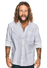 Wall Mural - Handsome man with beard and long hair wearing casual clothes sticking tongue out happy with funny expression. emotion concept.