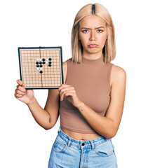 Wall Mural - Beautiful young blonde woman holding asian go game board depressed and worry for distress, crying angry and afraid. sad expression.