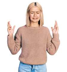 Poster - Beautiful young blonde woman wearing brown sweater gesturing finger crossed smiling with hope and eyes closed. luck and superstitious concept.