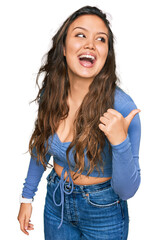 Wall Mural - Young hispanic girl wearing casual clothes smiling with happy face looking and pointing to the side with thumb up.