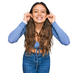 Wall Mural - Young hispanic girl wearing casual clothes smiling pulling ears with fingers, funny gesture. audition problem