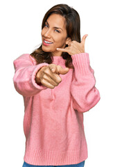 Wall Mural - Young hispanic woman wearing casual clothes smiling doing talking on the telephone gesture and pointing to you. call me.