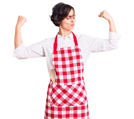 Poster - Beautiful young woman with short hair wearing professional cook apron showing arms muscles smiling proud. fitness concept.