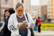 Latina adult woman, with a happy expression, in the city using her smartphone, sending audio messages and typing. Copyspace......