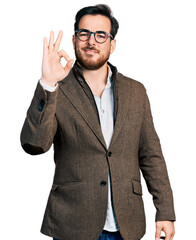 Wall Mural - Young hispanic man wearing business jacket and glasses smiling positive doing ok sign with hand and fingers. successful expression.