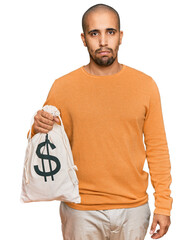 Poster - Hispanic adult man holding dollars bag thinking attitude and sober expression looking self confident