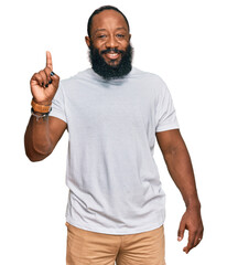 Poster - Young african american man wearing casual white tshirt showing and pointing up with finger number one while smiling confident and happy.