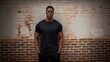 a handsome African American man wearing a blank black t-shirt, standing against a brick wall,