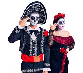 Poster - Young couple wearing mexican day of the dead costume over background shooting and killing oneself pointing hand and fingers to head like gun, suicide gesture.