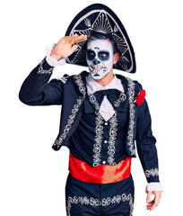 Canvas Print - Young man wearing day of the dead costume over background very happy and smiling looking far away with hand over head. searching concept.