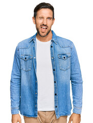 Canvas Print - Young handsome man wearing casual denim jacket winking looking at the camera with sexy expression, cheerful and happy face.