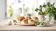  a plate of rolls sitting on top of a table next to a bowl of broccoli and a vase of flowers.