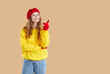 Cheerful woman pointing with finger on copy space for autumn seasonal offer or promotional deal. Woman in beret, gloves and sweatshirt pointing index finger at empty copy space on beige background.