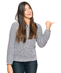 Canvas Print - Young brunette woman wearing casual winter sweater smiling with happy face looking and pointing to the side with thumb up.