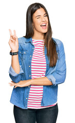 Wall Mural - Young brunette woman wearing casual clothes smiling with happy face winking at the camera doing victory sign with fingers. number two.