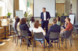 © Studio Romantic - Business meeting. Serious business group leader instructing team, telling project strategy and presenting tasks. Confident man is talking to colleagues sitting in circle at meeting in office.