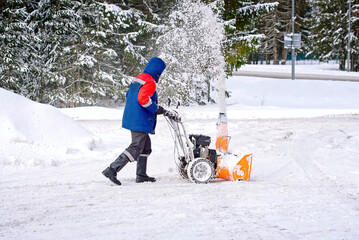 Wall Mural - Man with petrol snow blower clearing snow and ice on parking area. Worker removing snow with portable snowthrower machine. Clean sidewalk from snow. Man operating snow blower