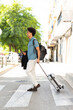 © mimagephotos - Full body young traveler crosses a city street with a suitcase