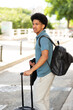 © mimagephotos - young man poses for a relaxed portrait, suitcase by his side