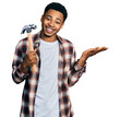 © Krakenimages.com - Young african american man holding hammer celebrating achievement with happy smile and winner expression with raised hand