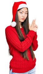 Wall Mural - Young chinese woman wearing christmas hat holding symbolic gun with hand gesture, playing killing shooting weapons, angry face