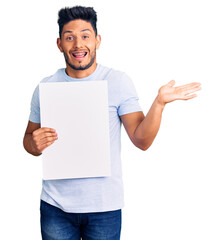 Sticker - Handsome latin american young man holding cardboard banner with blank space celebrating victory with happy smile and winner expression with raised hands