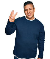 Wall Mural - Young latin man wearing casual clothes showing and pointing up with fingers number three while smiling confident and happy.