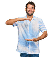 Canvas Print - Handsome young man with beard wearing casual fresh shirt gesturing with hands showing big and large size sign, measure symbol. smiling looking at the camera. measuring concept.