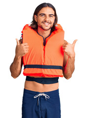 Young handsome man wearing nautical lifejacket success sign doing positive gesture with hand, thumbs up smiling and happy. cheerful expression and winner gesture.