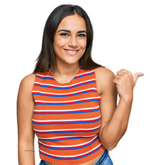 Wall Mural - Young brunette woman wearing casual clothes smiling with happy face looking and pointing to the side with thumb up.