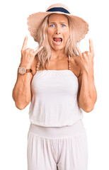 Wall Mural - Middle age fit blonde woman wearing summer hat shouting with crazy expression doing rock symbol with hands up. music star. heavy concept.